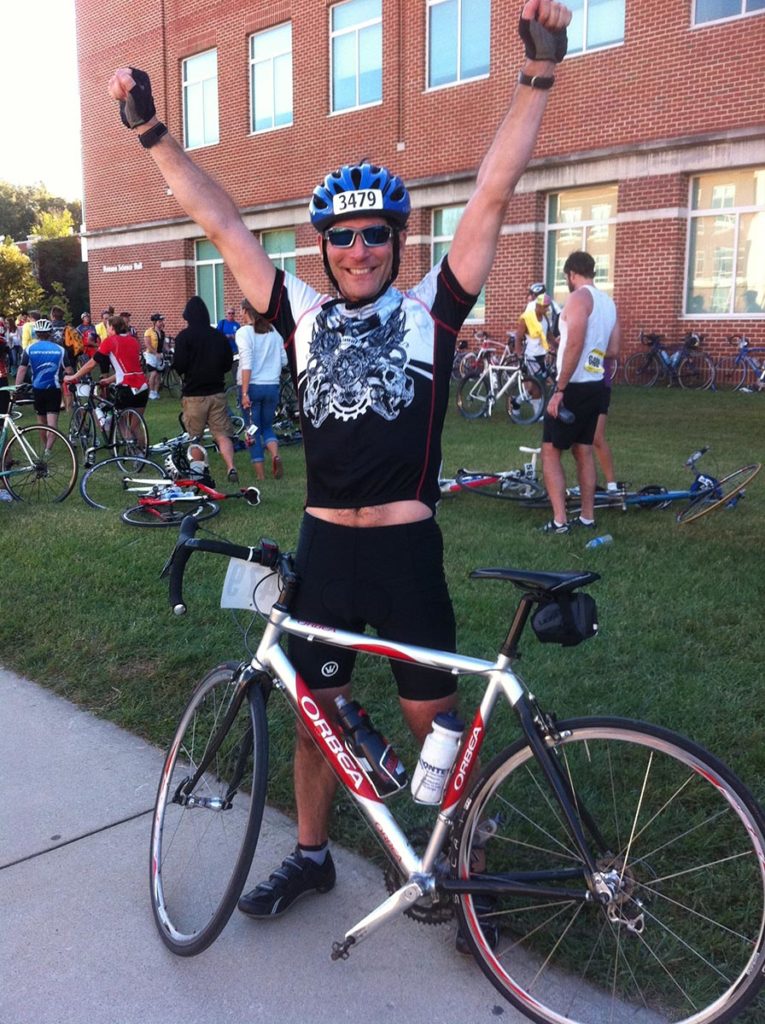 Bicyclist standing next to bike with arms raised in celebration