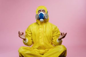 Person in a yellow hazmat suit with respirator sitting in a meditation pose.  